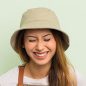 A woman with long hair wearing a beige bucket hat and a white shirt smiles brightly with her eyes closed against a light green background, reflecting the cheerful spirit of Cordes Family Landscaping and Snow LLC.