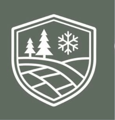 A white shield emblem on a green background featuring two pine trees, a snowflake, and curved lines representing a landscape or road.